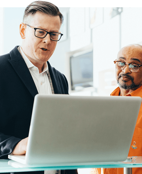 Two professionals are discussing something while looking at a laptop screen in a bright office setting